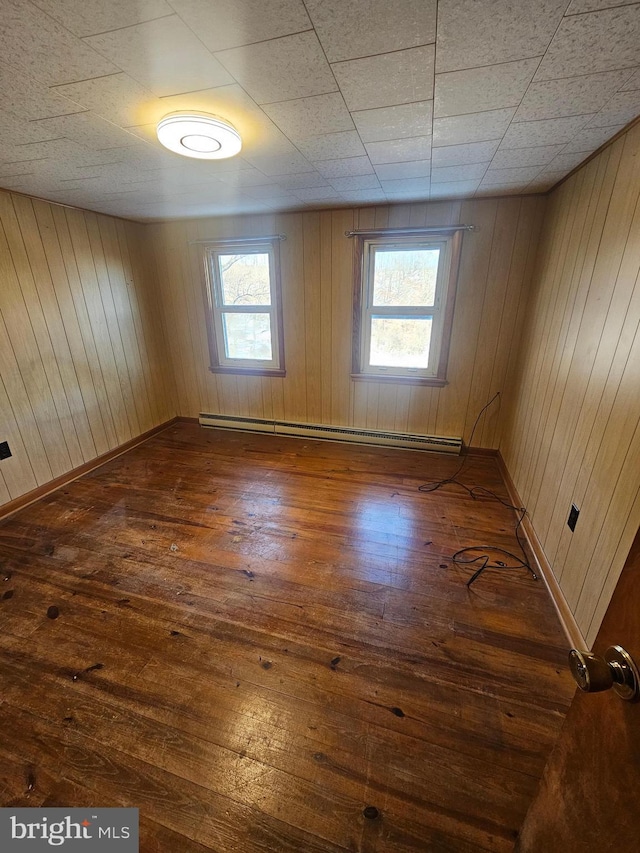 empty room with a baseboard heating unit, dark wood-type flooring, and wooden walls