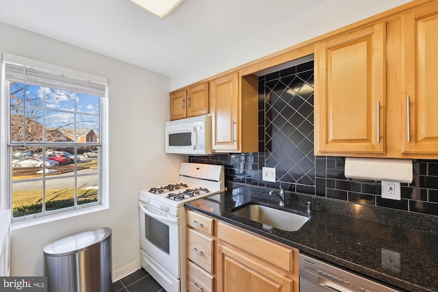 kitchen with sink, white appliances, backsplash, dark tile patterned flooring, and dark stone counters