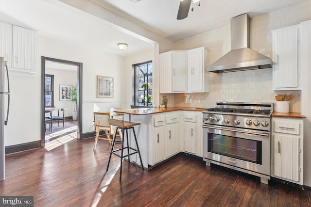 kitchen with high end range, kitchen peninsula, wall chimney range hood, decorative backsplash, and white cabinets