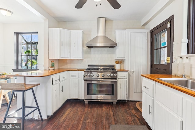 kitchen with white cabinetry, stainless steel range, a kitchen bar, kitchen peninsula, and wall chimney exhaust hood