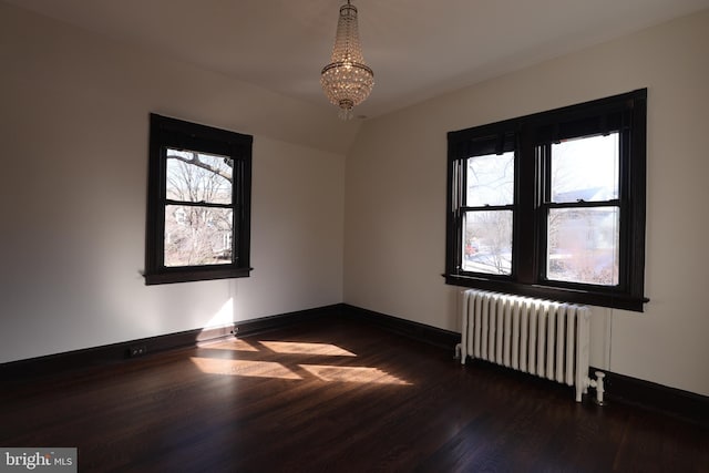 empty room featuring dark hardwood / wood-style flooring, a wealth of natural light, radiator heating unit, and a chandelier