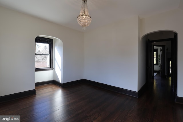 empty room with dark wood-type flooring and a chandelier