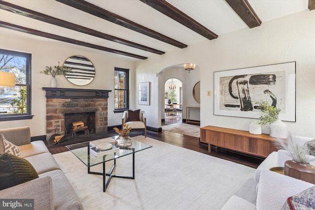 living room with beamed ceiling, wood-type flooring, an inviting chandelier, and a fireplace