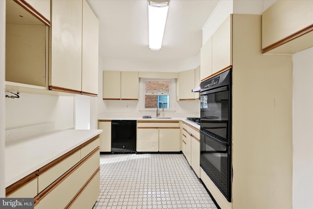kitchen with black appliances, cream cabinetry, light countertops, light floors, and a sink