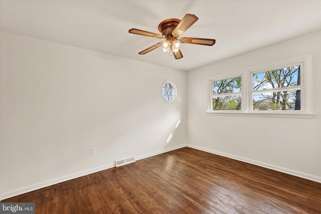 spare room with baseboards, dark wood-style floors, and a ceiling fan