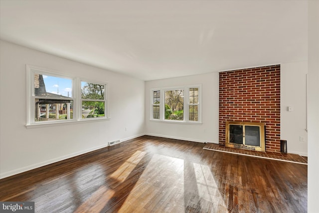 unfurnished living room with wood finished floors, baseboards, and a brick fireplace