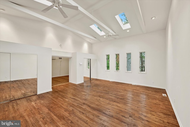 unfurnished room with a skylight, beam ceiling, high vaulted ceiling, a ceiling fan, and wood finished floors