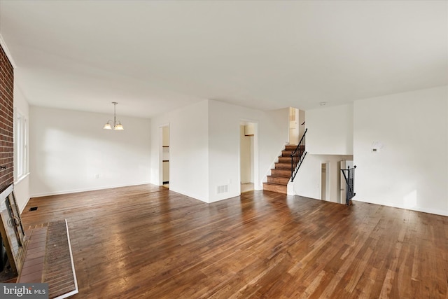 unfurnished living room featuring a fireplace, a chandelier, wood finished floors, and stairway