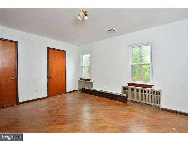 unfurnished room featuring radiator, a wealth of natural light, and hardwood / wood-style floors