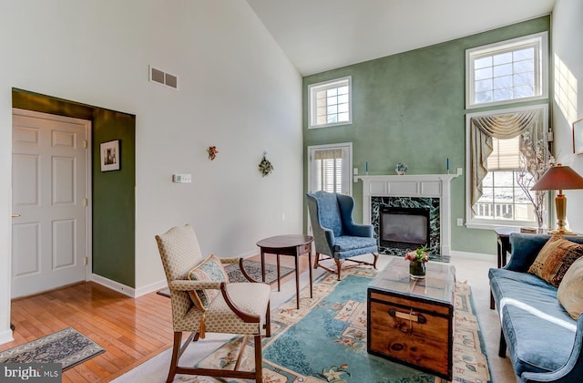 living room featuring a premium fireplace, a towering ceiling, and light hardwood / wood-style floors