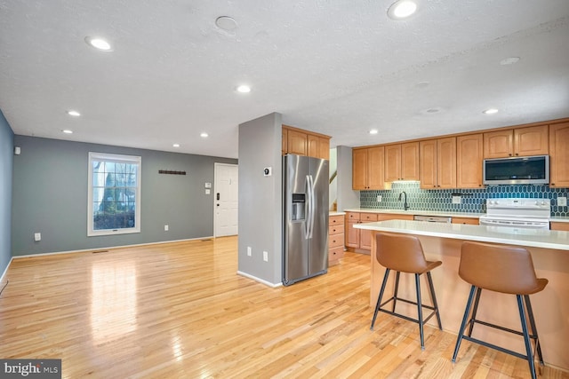 kitchen with appliances with stainless steel finishes, sink, backsplash, a kitchen breakfast bar, and light hardwood / wood-style floors