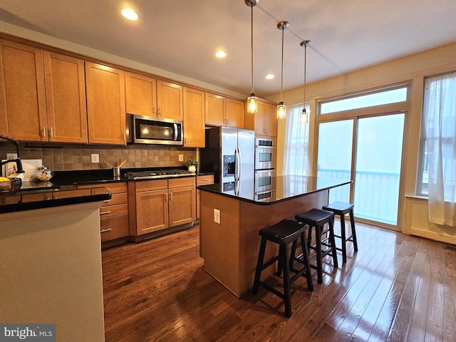 kitchen featuring a kitchen island, appliances with stainless steel finishes, dark hardwood / wood-style floors, backsplash, and hanging light fixtures