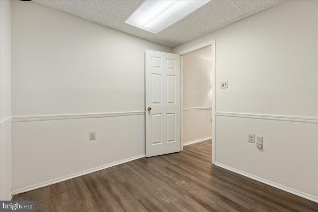 spare room with a paneled ceiling and dark hardwood / wood-style flooring