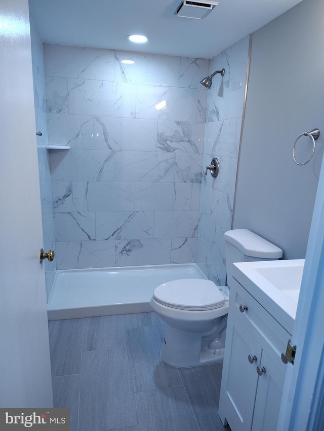 full bathroom with vanity, toilet, visible vents, and a tile shower