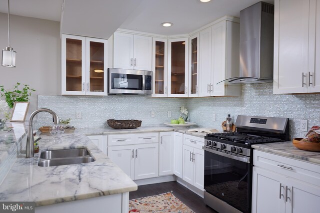 kitchen with stainless steel appliances, wall chimney exhaust hood, a sink, light stone counters, and white cabinetry