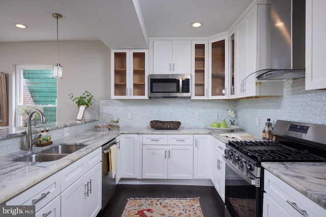 kitchen with wall chimney range hood, appliances with stainless steel finishes, a sink, white cabinetry, and recessed lighting