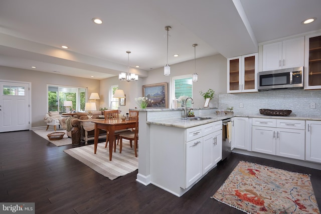 kitchen featuring a sink, stainless steel appliances, a peninsula, tasteful backsplash, and glass insert cabinets