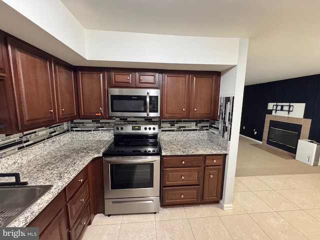 kitchen with stainless steel appliances, a tile fireplace, sink, and light tile patterned floors