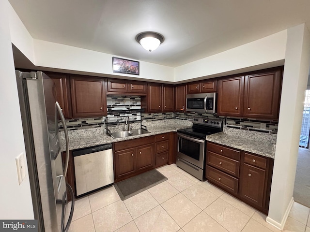 kitchen with sink, light tile patterned floors, appliances with stainless steel finishes, light stone countertops, and decorative backsplash