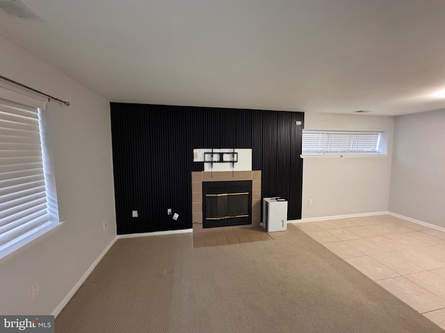 unfurnished living room featuring a tiled fireplace, light tile patterned floors, and a wealth of natural light