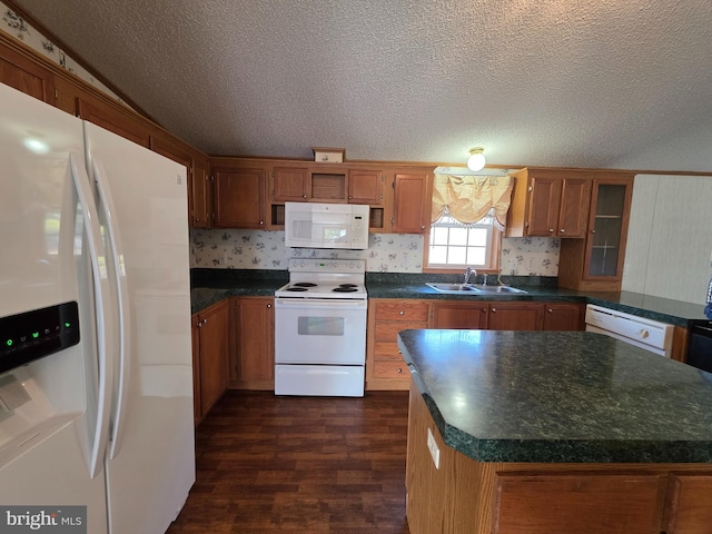 kitchen with white appliances, dark wood finished floors, brown cabinetry, dark countertops, and a sink