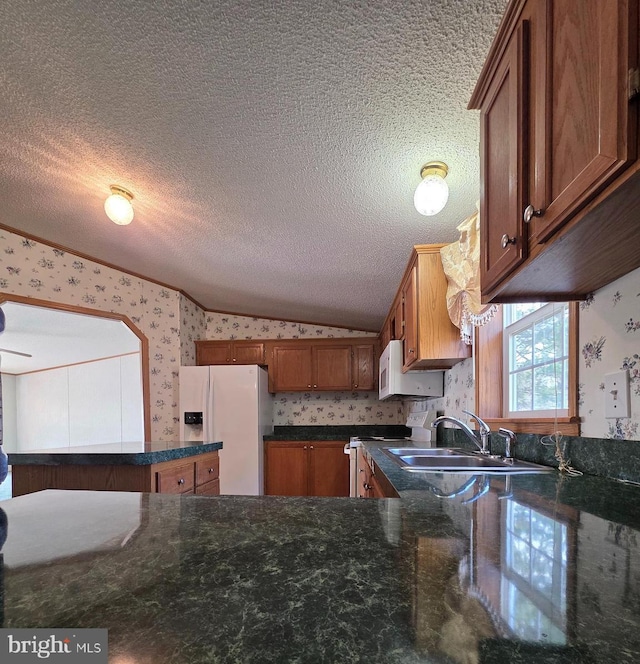 kitchen featuring lofted ceiling, brown cabinetry, a textured ceiling, white appliances, and wallpapered walls