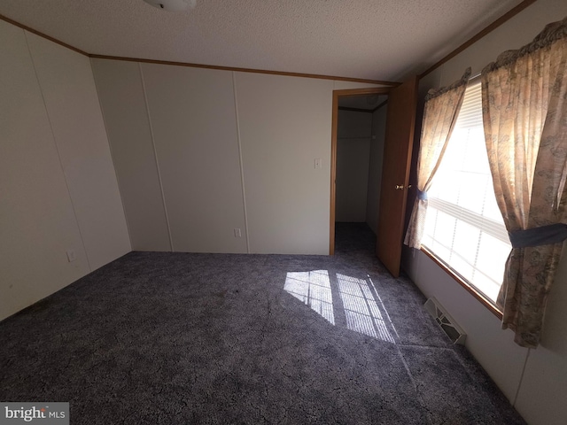 empty room featuring a textured ceiling, ornamental molding, carpet, and visible vents