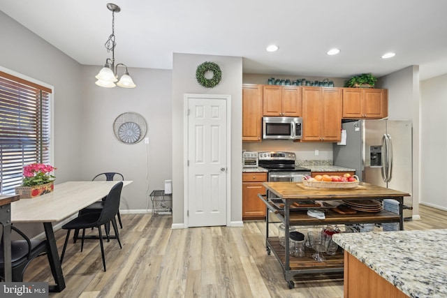 kitchen featuring an inviting chandelier, hanging light fixtures, appliances with stainless steel finishes, light stone countertops, and light hardwood / wood-style floors