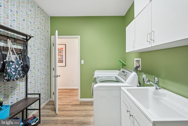 clothes washing area with cabinets, washing machine and clothes dryer, sink, and light wood-type flooring