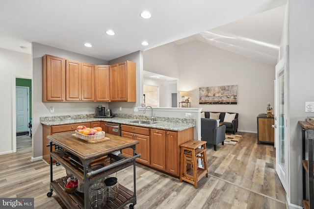 kitchen with lofted ceiling, light stone countertops, sink, and light hardwood / wood-style flooring