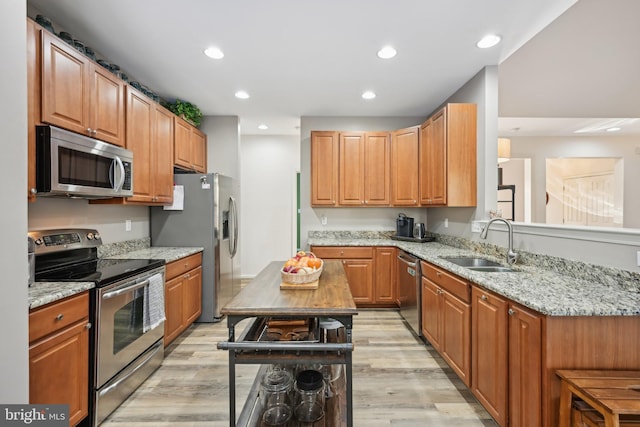 kitchen with a kitchen island, appliances with stainless steel finishes, sink, light stone countertops, and light hardwood / wood-style flooring