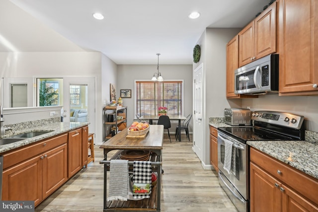 kitchen with appliances with stainless steel finishes, pendant lighting, sink, light stone countertops, and light wood-type flooring