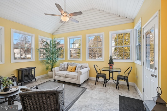 sunroom with plenty of natural light, vaulted ceiling, and a wood stove