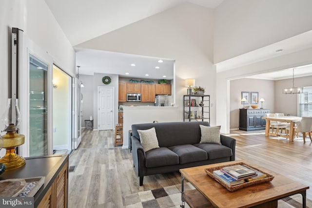 living room with an inviting chandelier, high vaulted ceiling, and light hardwood / wood-style floors