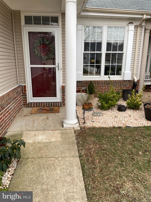 property entrance featuring roof with shingles and brick siding