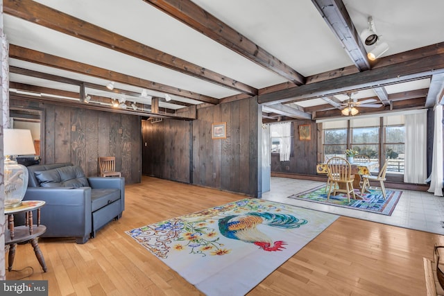 living room with beam ceiling, ceiling fan, wooden walls, and light hardwood / wood-style floors