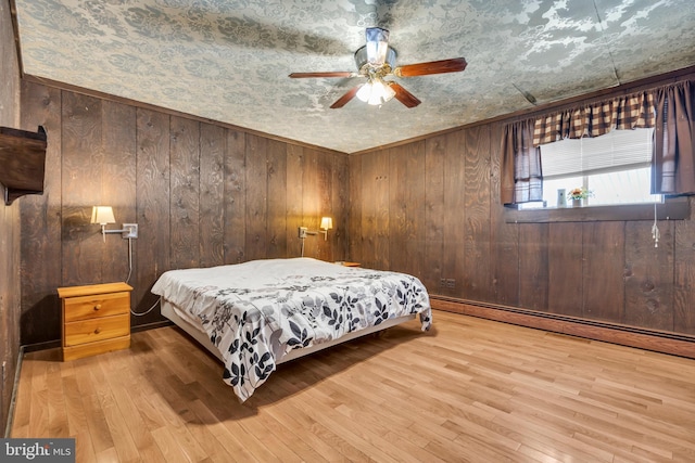 bedroom with baseboard heating, wood walls, ceiling fan, and light hardwood / wood-style floors