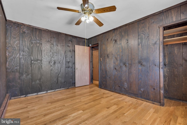 unfurnished bedroom with baseboard heating, light wood-type flooring, ceiling fan, and wood walls