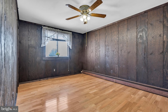 empty room with baseboard heating, light hardwood / wood-style floors, ceiling fan, and wood walls