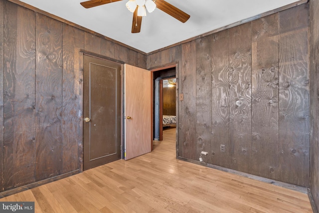 empty room with ceiling fan, light hardwood / wood-style floors, and wood walls