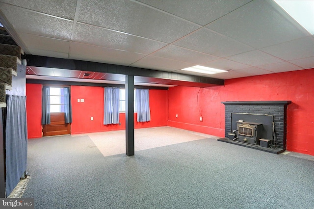 basement featuring a paneled ceiling, a wood stove, and carpet