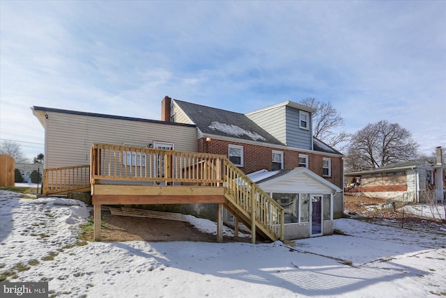 snow covered back of property featuring a wooden deck and a sunroom