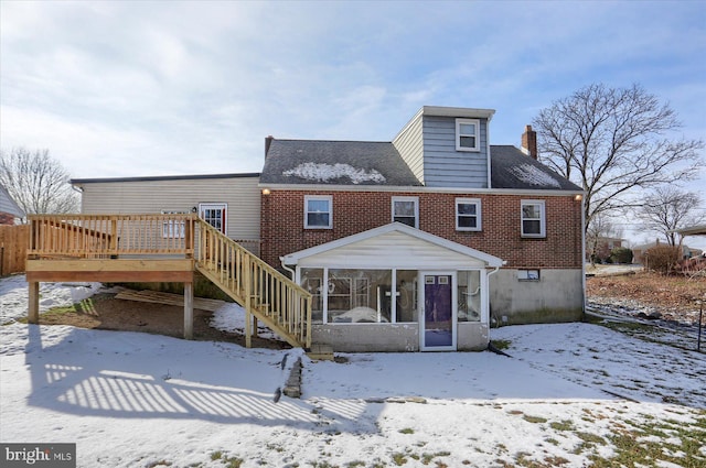 snow covered back of property featuring a wooden deck and a sunroom