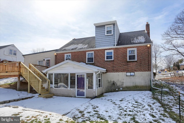 snow covered back of property with a wooden deck and a sunroom