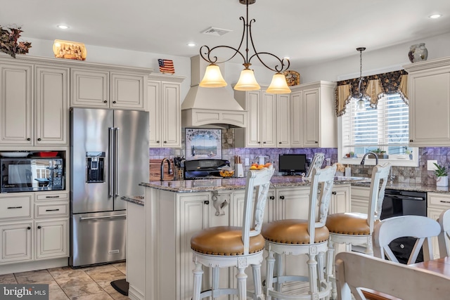 kitchen featuring premium range hood, high end fridge, backsplash, light stone countertops, and decorative light fixtures