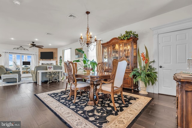 dining space with ceiling fan with notable chandelier and dark hardwood / wood-style flooring