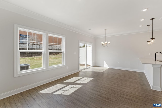 unfurnished living room with a notable chandelier, dark wood-type flooring, ornamental molding, and sink