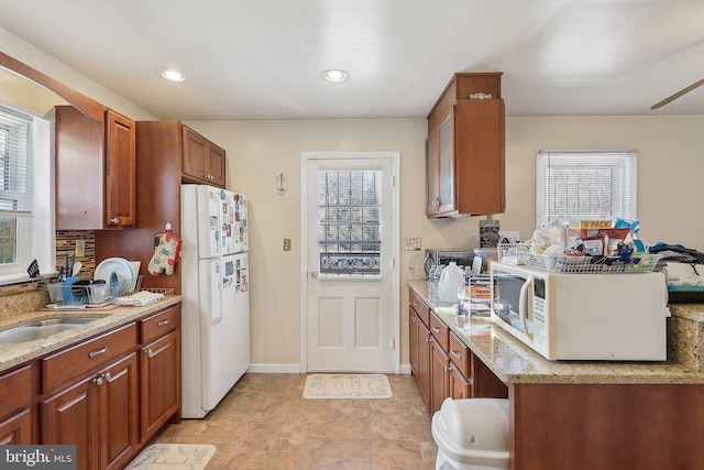 kitchen featuring light stone counters, white appliances, and sink