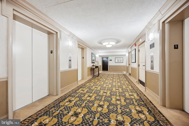 corridor featuring crown molding, light carpet, elevator, and a textured ceiling