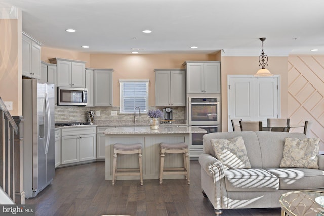 kitchen featuring a kitchen island, appliances with stainless steel finishes, pendant lighting, a kitchen breakfast bar, and light stone counters